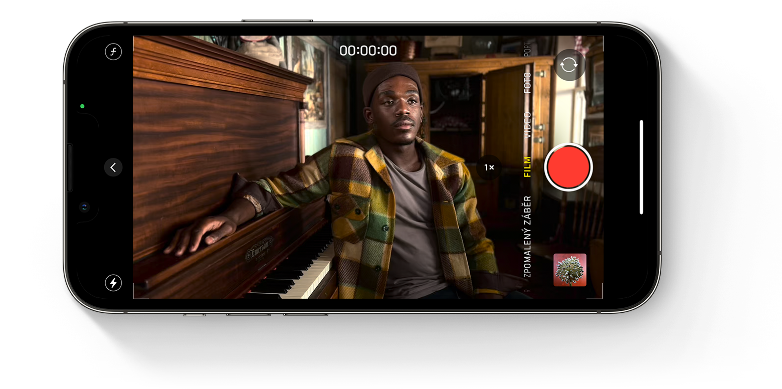 Obrazovka iPhonu zobrazující osobu sedící u klavíru se spuštěnou aplikací Fotoaparát ve filmařském režimu